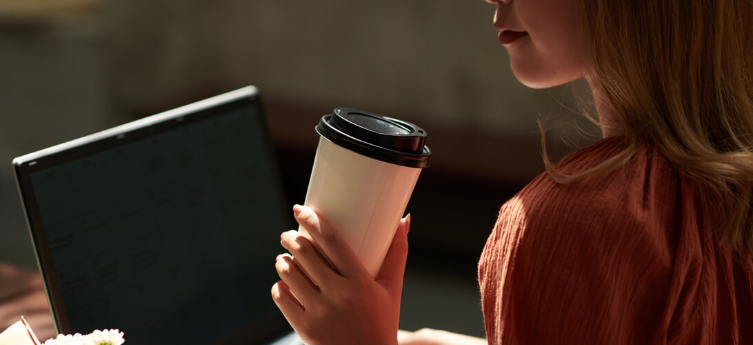 Profissional com copo de café em uma mão e olhando para computador