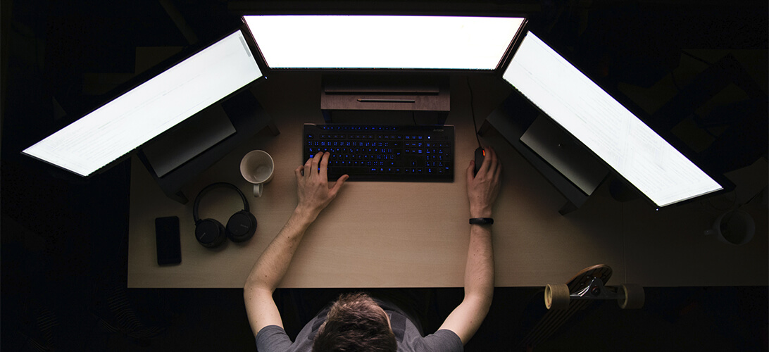 Visão aérea de pessoa utilizando computador com três monitores em sua frente